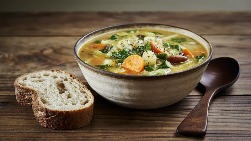 Ciotola di minestrone rustico con verdure e fagioli accanto a pane integrale